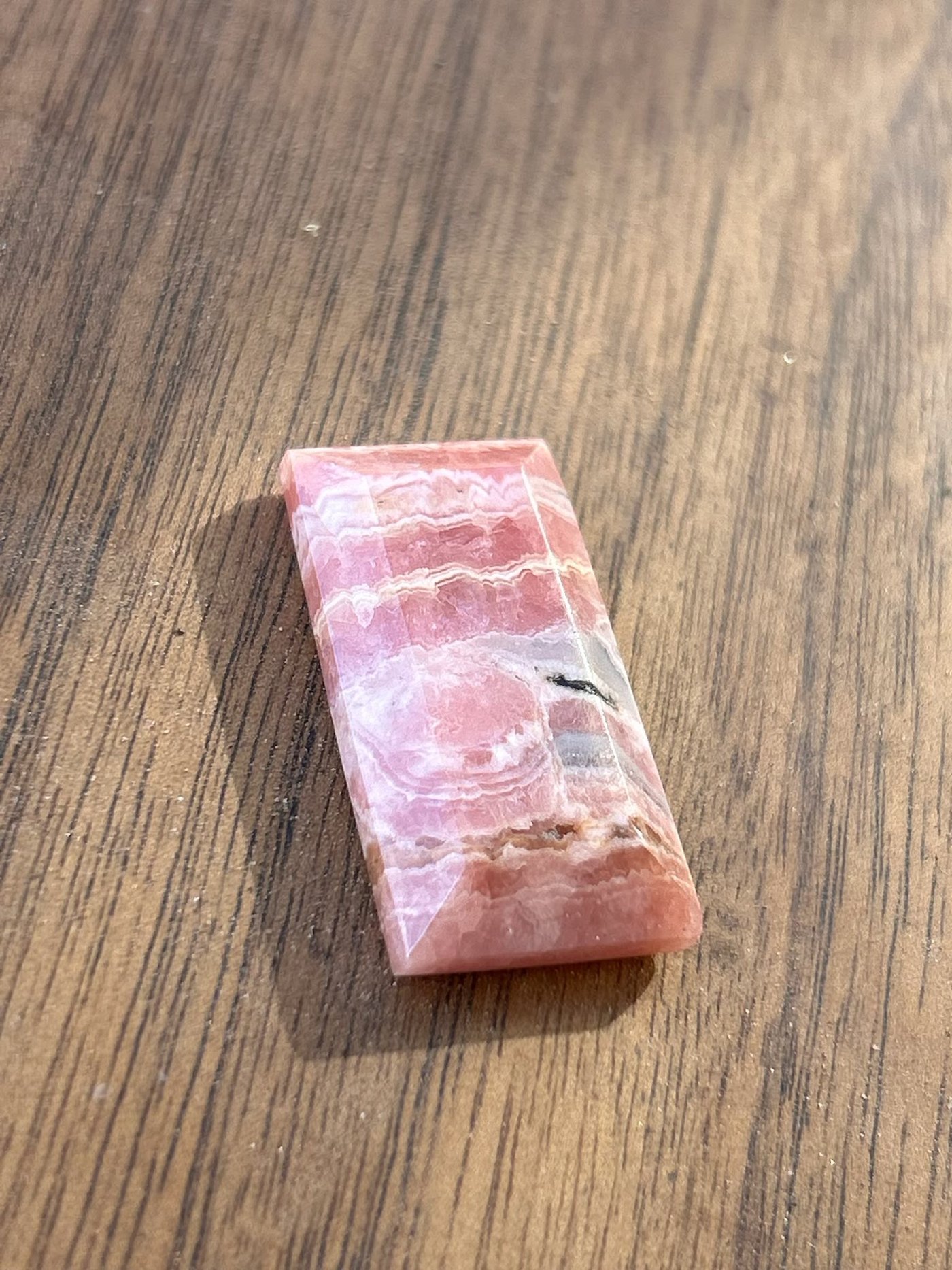 A rectangular stone banded in rose pink and white, cut with a stepped edge, on a wooden bench top.