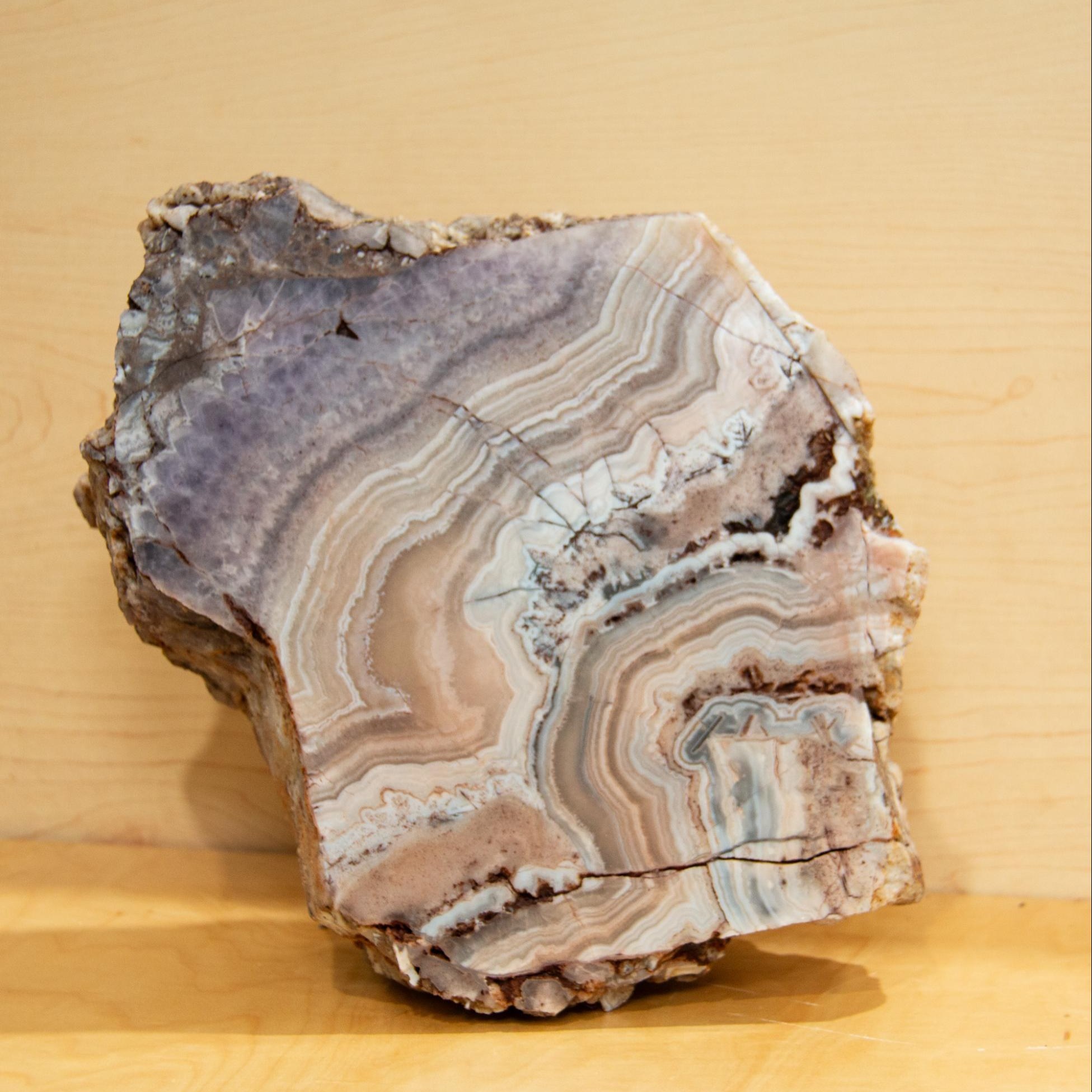 A rough stone with one face cut open, showing violet and cream banding inside a crusted rind.