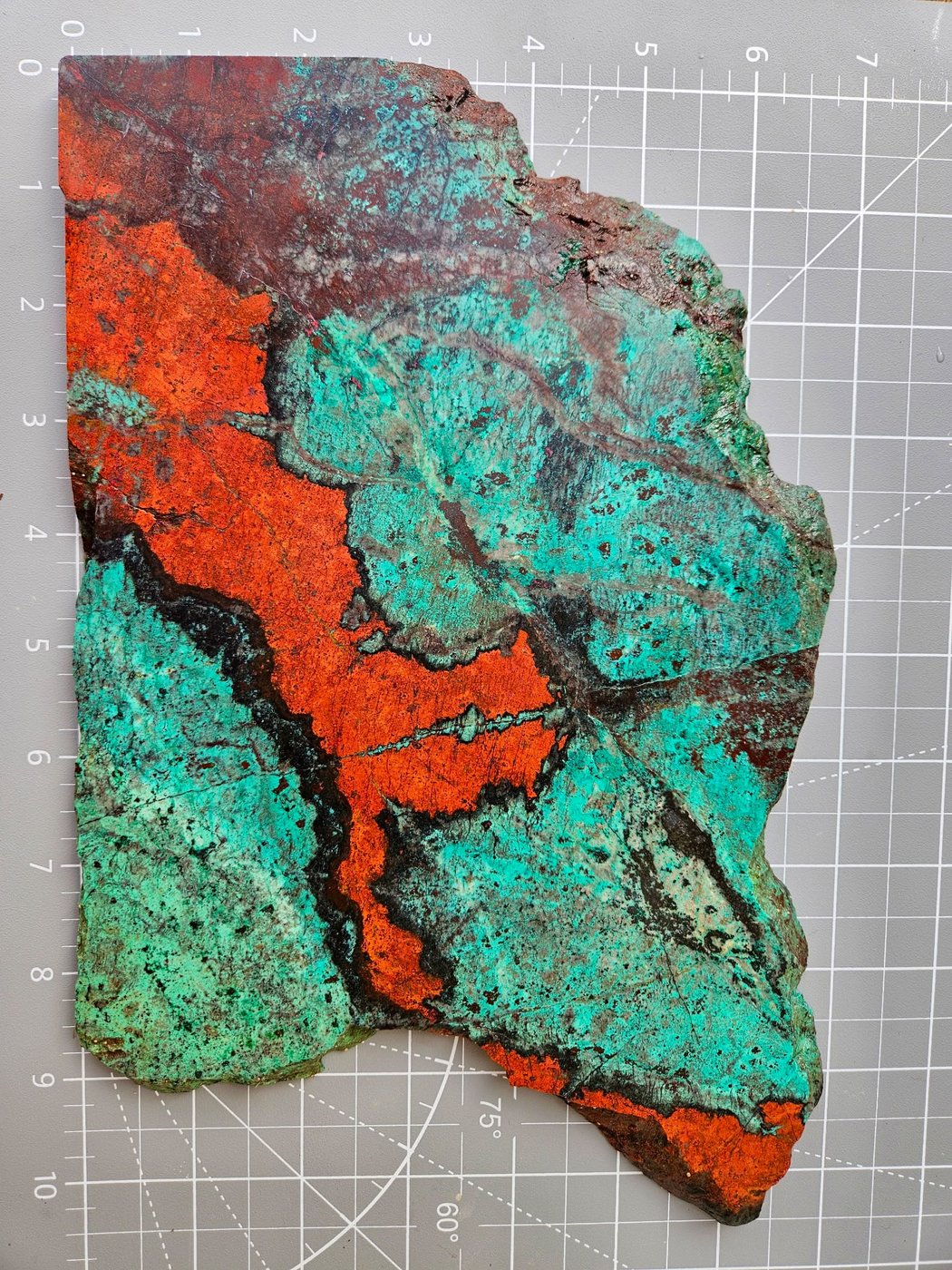 A second Sonoran sunrise slab on the same gridded mat, broader fields of blue green chrysocolla with orange red cuprite running corner to corner.