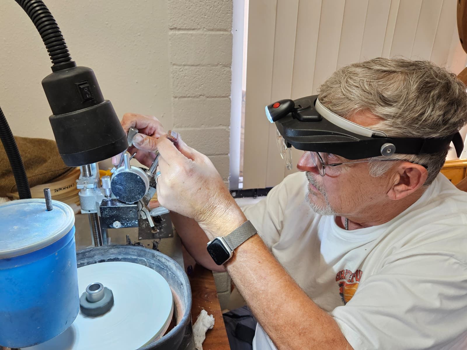 Les at the flat lap, holding a dopped stone steady under a loupe headset.